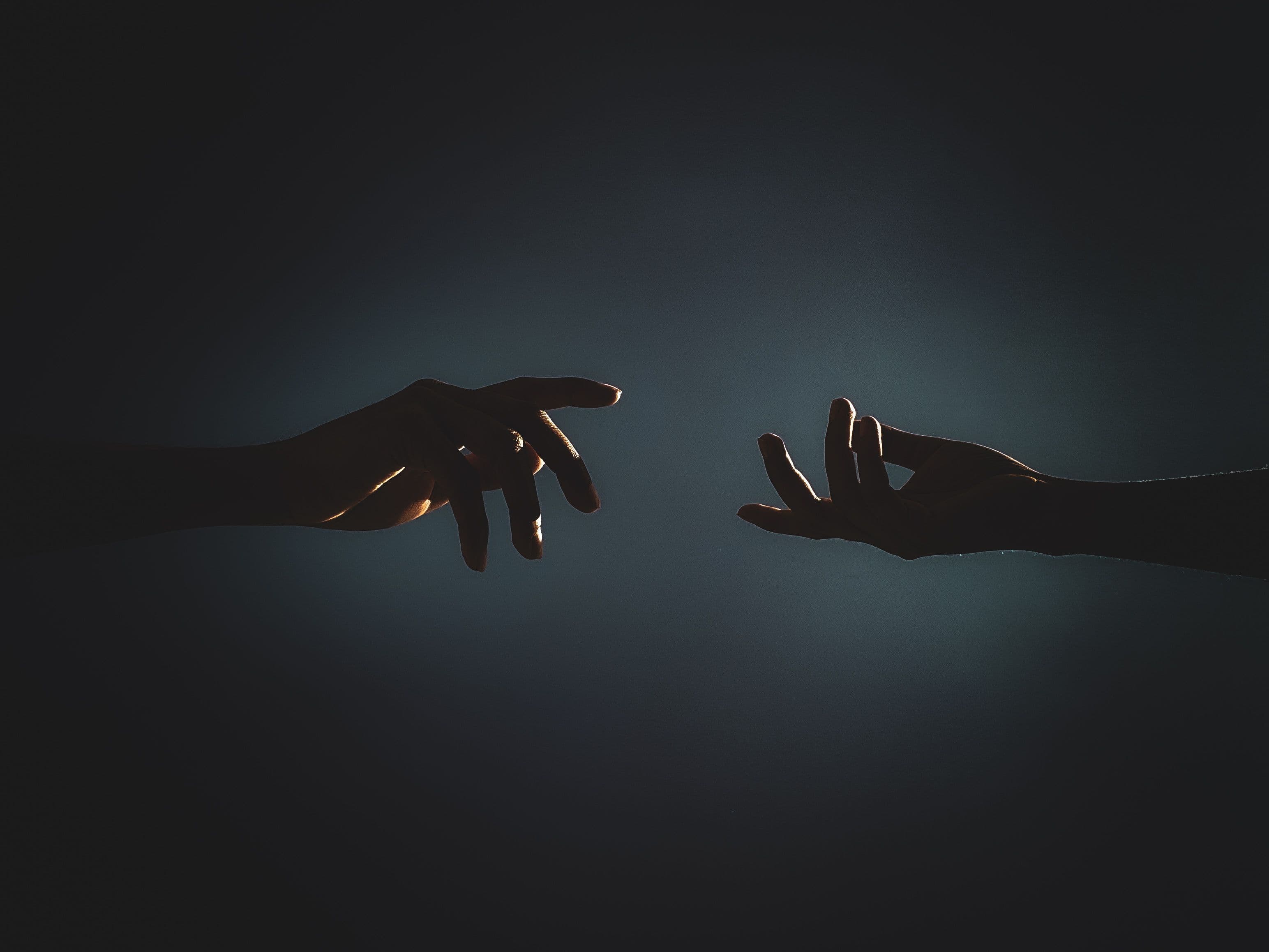 Two silhouetted hands reaching toward each other in darkness