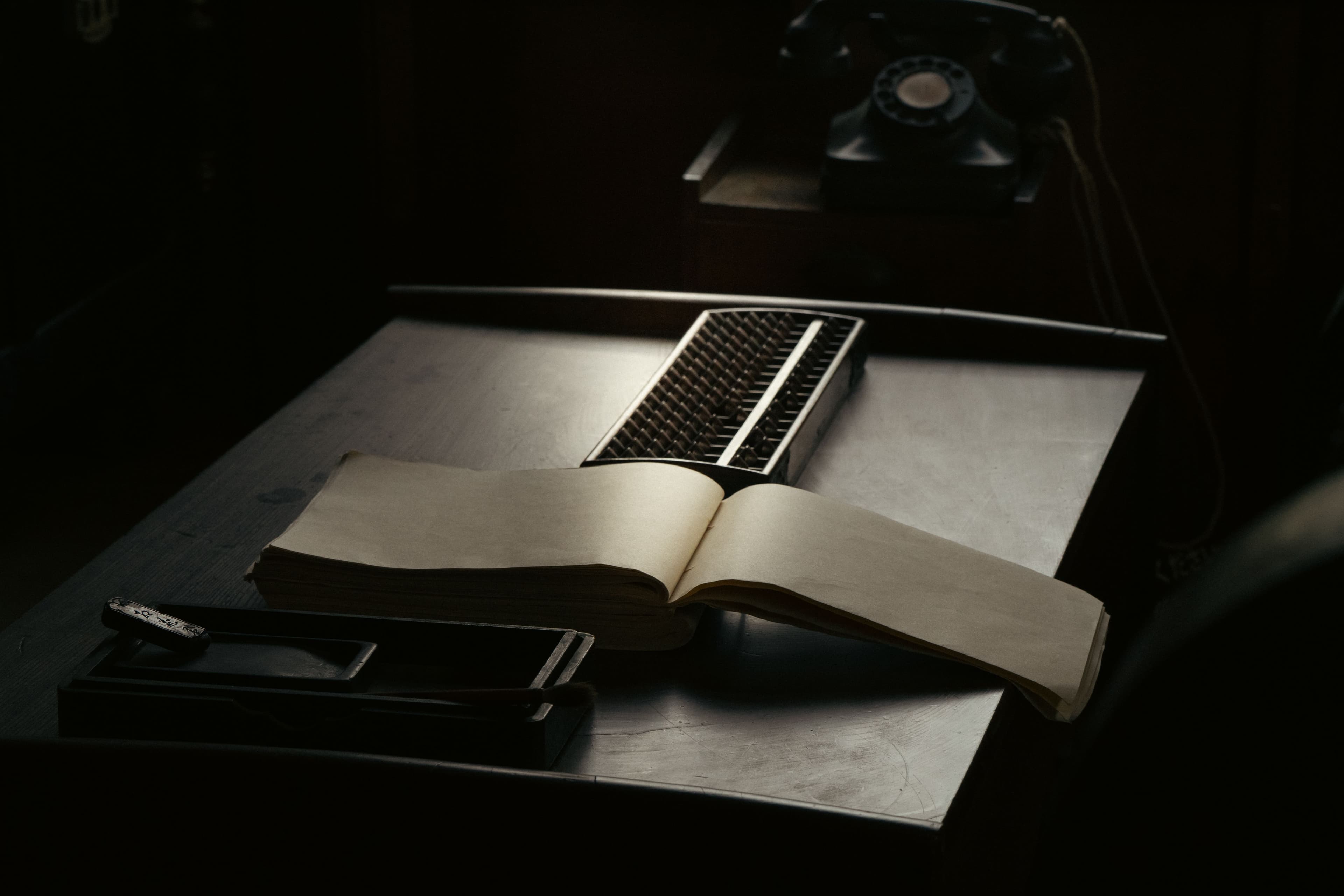 An open vintage ledger book on a dark desk beside an old telephone